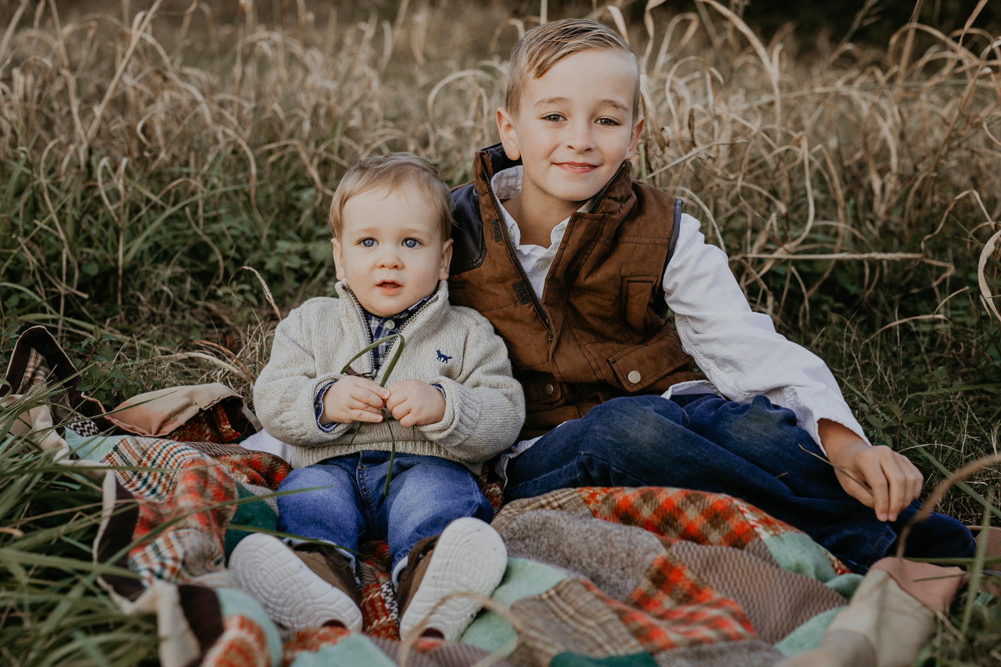 Two young brothers sit on a blanket in a field during spring hill family photos. 