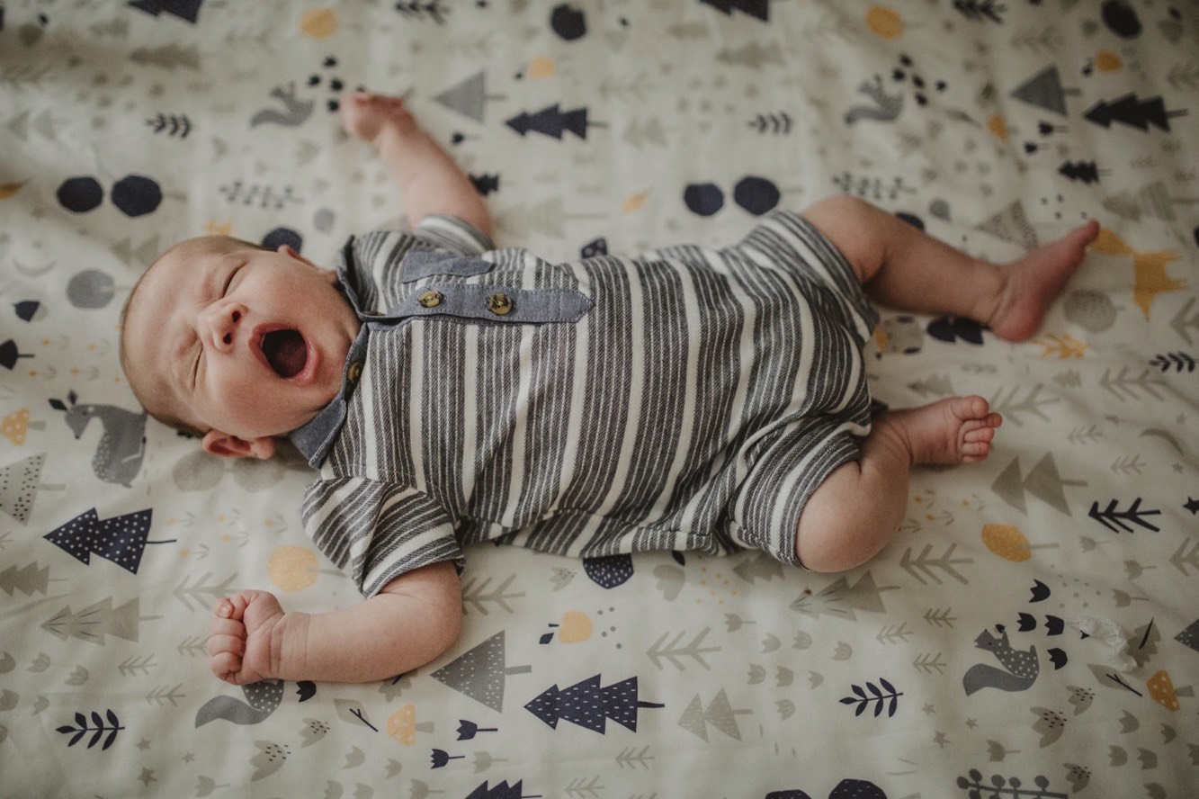 Newborn boy lays in his crib with a large yawn.