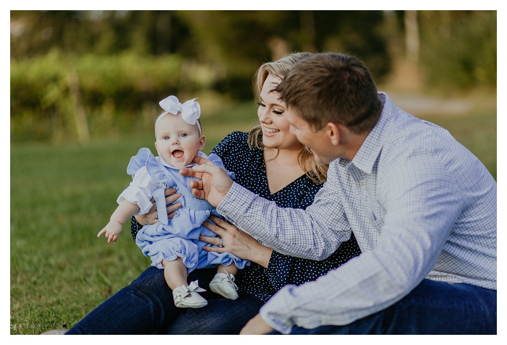 baby girl on mom's knee while dad makes her giggle by Nashville family photographer