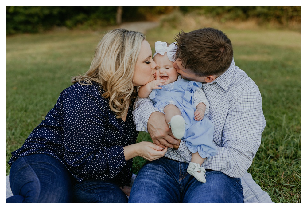 both parents kiss baby girl in the middle by Nashville family photographer
