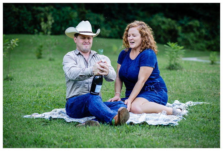 cowboy tries to pop champagne bottle, nashville engagement, nashville engagement photographer, Spring Hill Tennessee, outdoor engagement photos, field engagement photos, cowboy hat, cowboy, western engagement photos, Spring Hill engagement photographer, cowboy and cowgirl, summer engagement photos