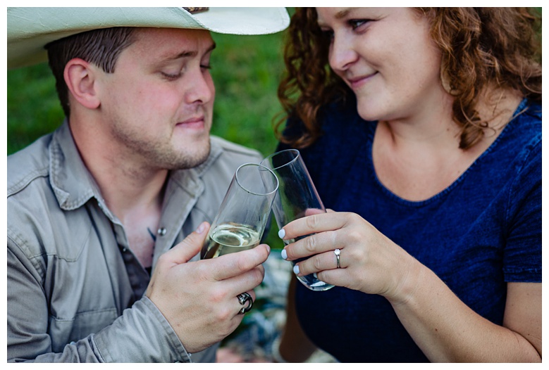 engaged couple toast with champagne glasses, nashville engagement, nashville engagement photographer, Spring Hill Tennessee, outdoor engagement photos, field engagement photos, cowboy hat, cowboy, western engagement photos, Spring Hill engagement photographer, cowboy and cowgirl, summer engagement photos