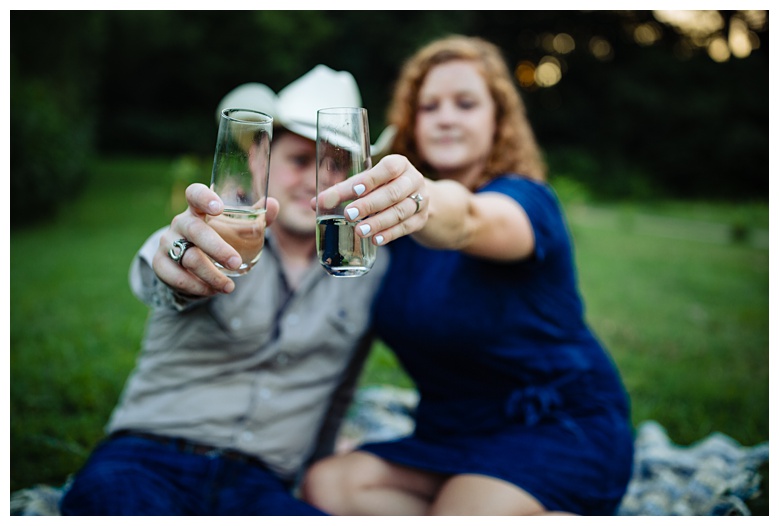 engaged couple hold their champagne glasses, nashville engagement, nashville engagement photographer, Spring Hill Tennessee, outdoor engagement photos, field engagement photos, cowboy hat, cowboy, western engagement photos, Spring Hill engagement photographer, cowboy and cowgirl, summer engagement photos