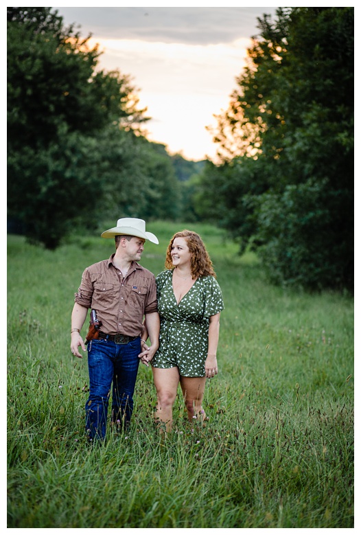 cowboy and cowgirl walk with sunset behind them, nashville engagement, nashville engagement photographer, Spring Hill Tennessee, outdoor engagement photos, field engagement photos, cowboy hat, cowboy, western engagement photos, Spring Hill engagement photographer, cowboy and cowgirl, summer engagement photos