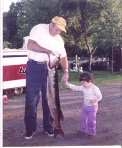 A grandfather holds a muskie fish while showing his little granddaughter