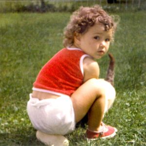 a little girl from the 1980s kneeling down on the ground petting a cat looking back over her shoulder.