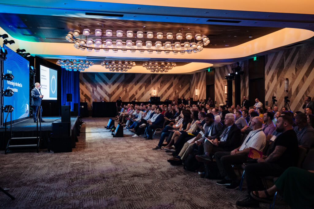 A wide photograph of the president of company, The Mercury Group, and the audience in attendance.